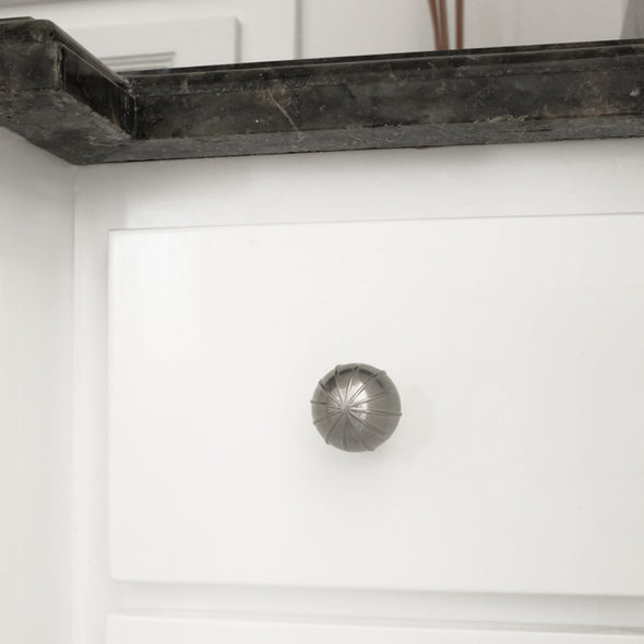 One Satin Nickel Hapny Sunburst knob installed on a small white drawer with a dark marble countertop