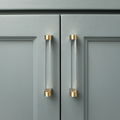 Two acrylic and brass 5" center to center luxury cabinet pulls in Clear Acrylic and Satin Brass installed on blue cabinet doors