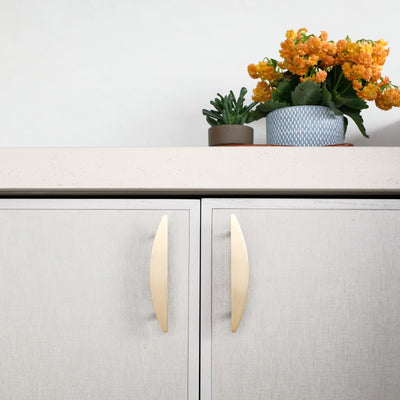 Two 4" Satin Brass Half Moon cabinet handles installed on tan cabinet doors.